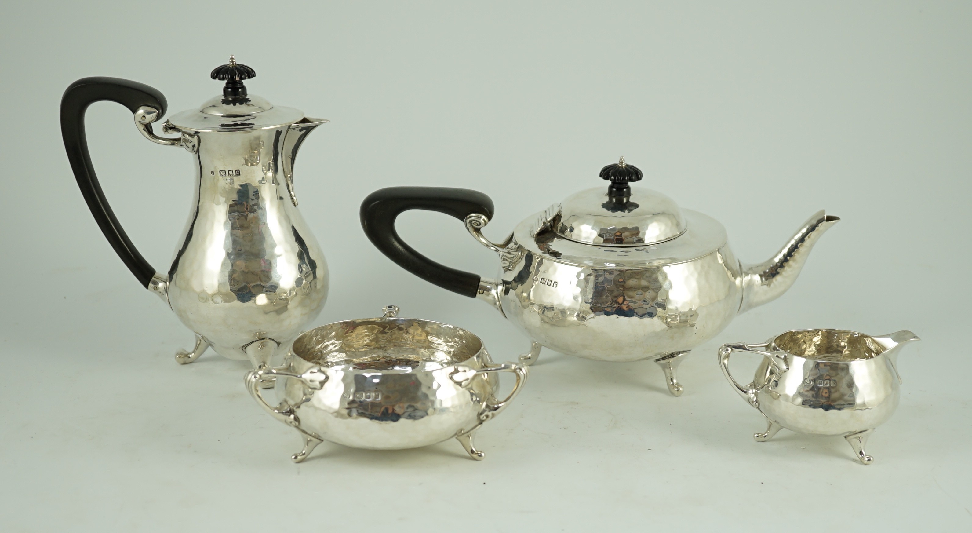 A George V Arts and Crafts three piece planished silver tea set and a similar hot water pot, by Charles Edwards